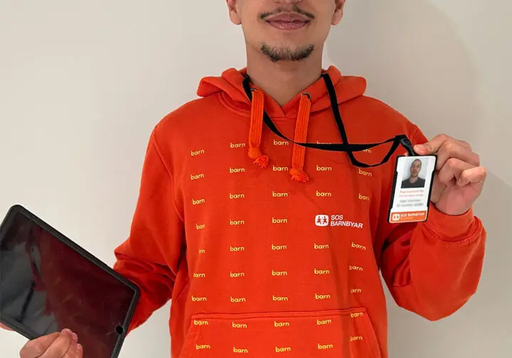 Representant för SOS Barnbyar iklädd orange luvtröja och ID-bricka.