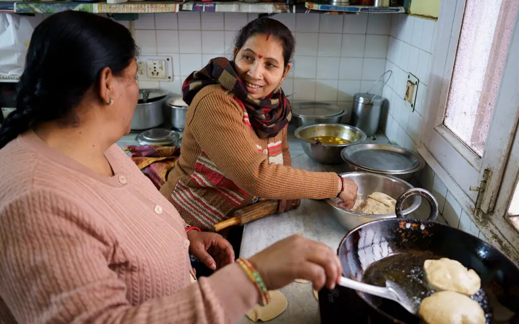 Indisk kvinna i brun kofta lagar mat med annan kvinna