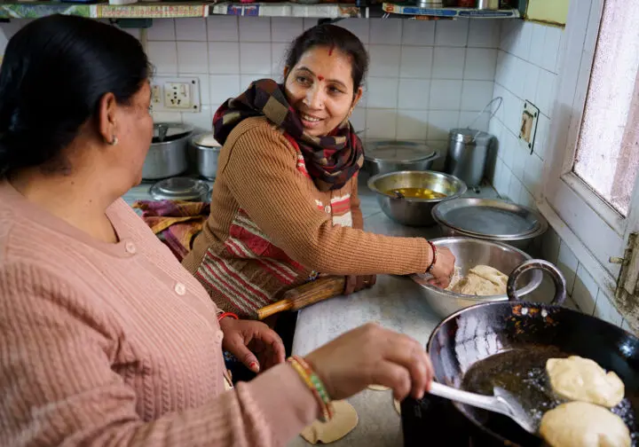 Indisk kvinna i brun kofta lagar mat med annan kvinna