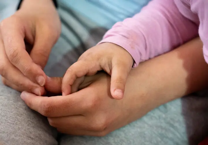 en barnhand håller i en trygg vuxenhand i knät