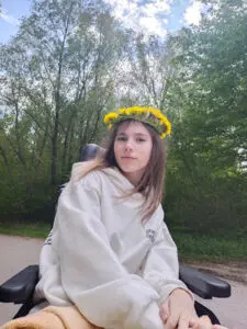 flicka utomhus i rullstol med gul blomsterkrans på huvudet