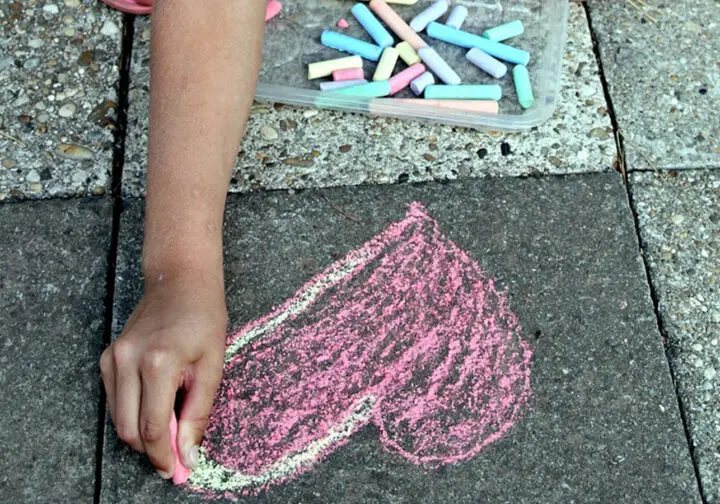 Barnhand ritar ett rosa hjärta i kriat på asfalt