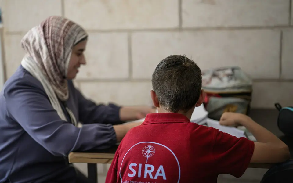 pojke i röd tröja bakifrån sitter och studerar med en kvinna