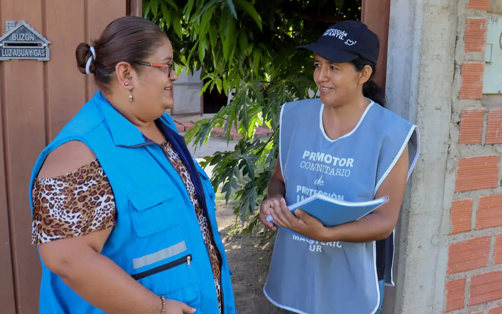 två kvinnor i blåa västar pratar med varandra