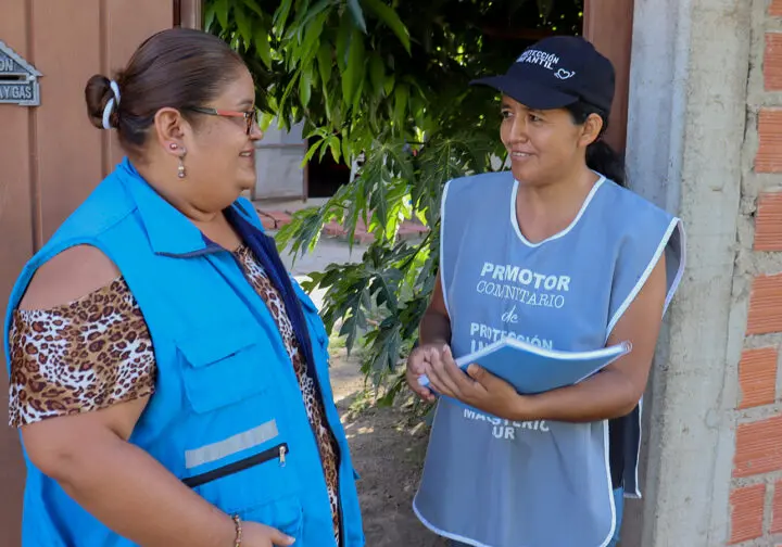 två kvinnor i blåa västar pratar med varandra