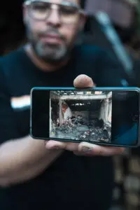 En man håller en mobilkamera som visar bild av nedbrunnet hus 