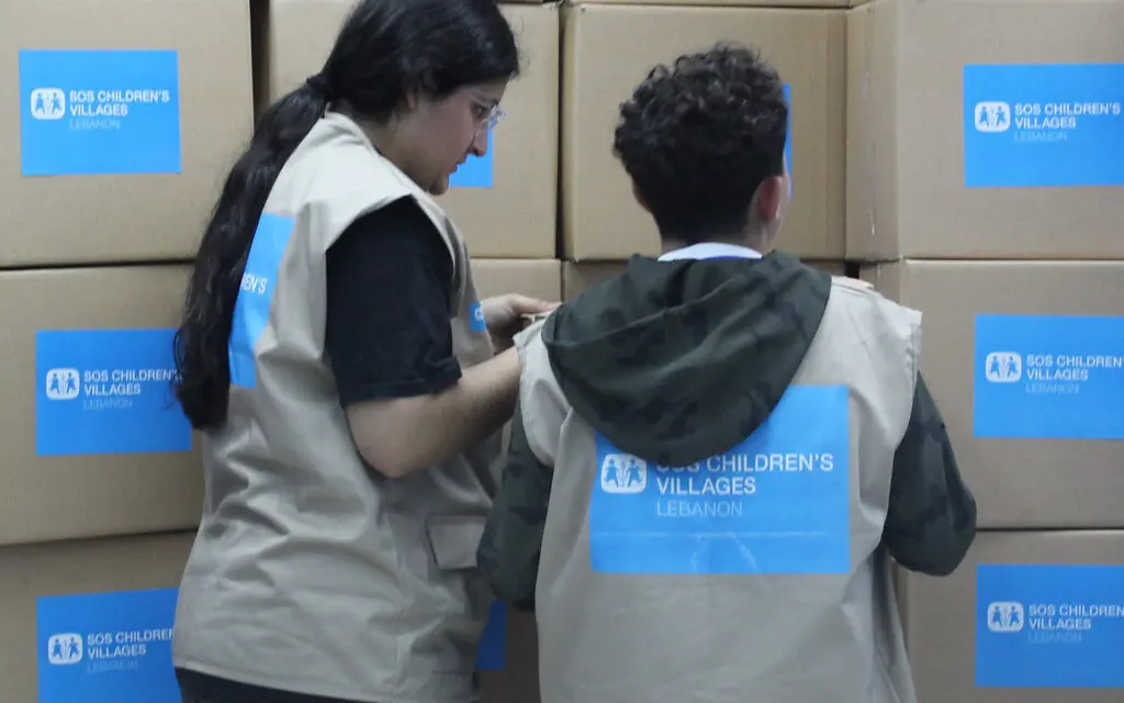 En vägg av kartonger med nödhjälp och två kvinnor i västar 