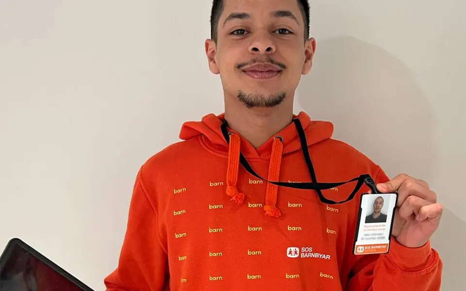 Representant för SOS Barnbyar iklädd orange luvtröja och ID-bricka.