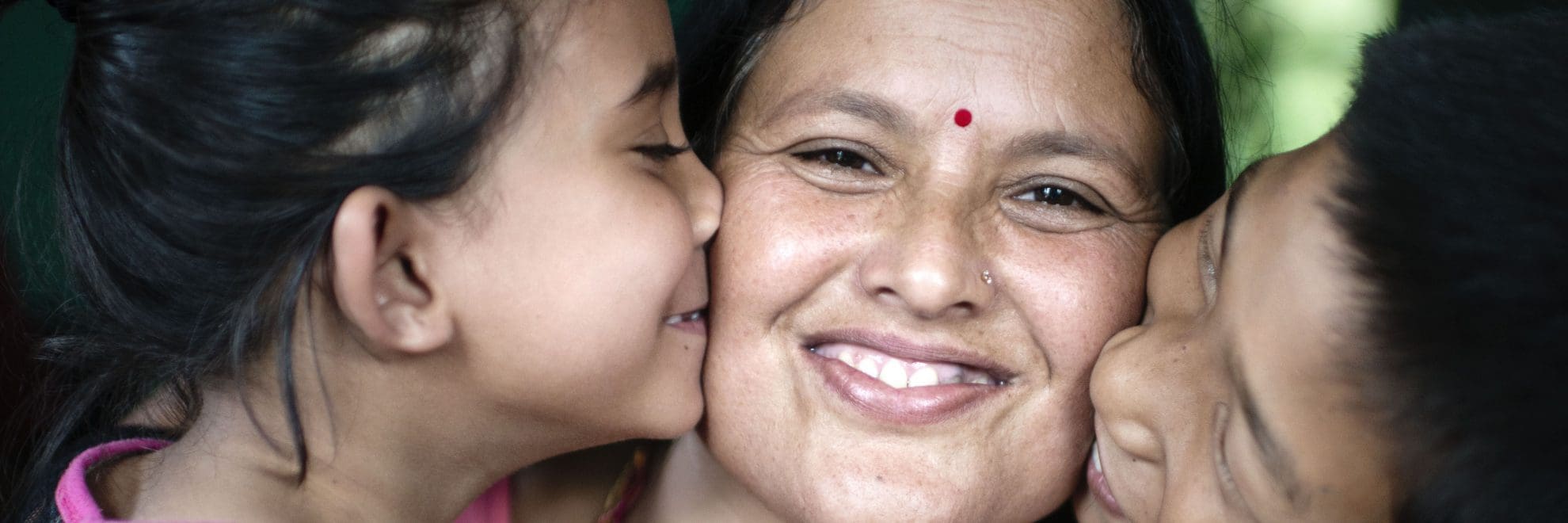 En mamma vars två fadderbarn pussar henne på kindeden och hon ser glad ut