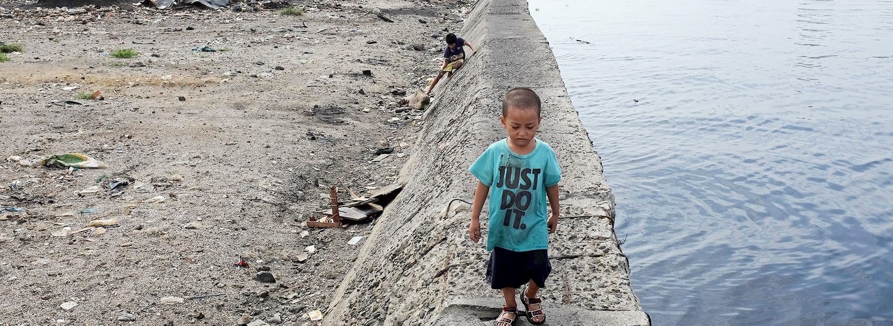 en liten pojke går på kanten av en stenmur som angränsar till havet.