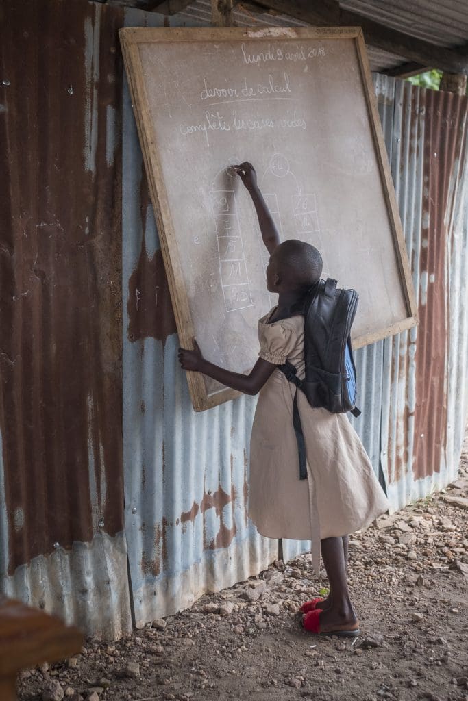 Flicka skriver på en svart tavla mot en vägg utomhus. 