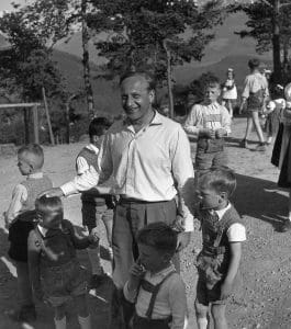Hermann Gmeiner, grundare av SOS Barnbyar, står utomhus omringad av barn.