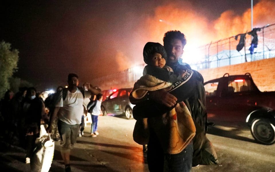 En man och ett barn som står framför en byggnad som brinner.