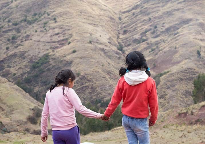 två flickor håller varandra i händerna medan de går bland gräsklädda berg.