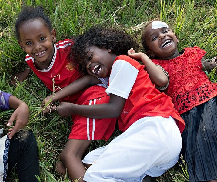 tre barn med röda t-shirts ligger i gräset och skrattar.