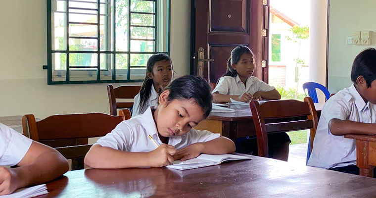 En flicka som sitter och skriver i ett klassrum.
