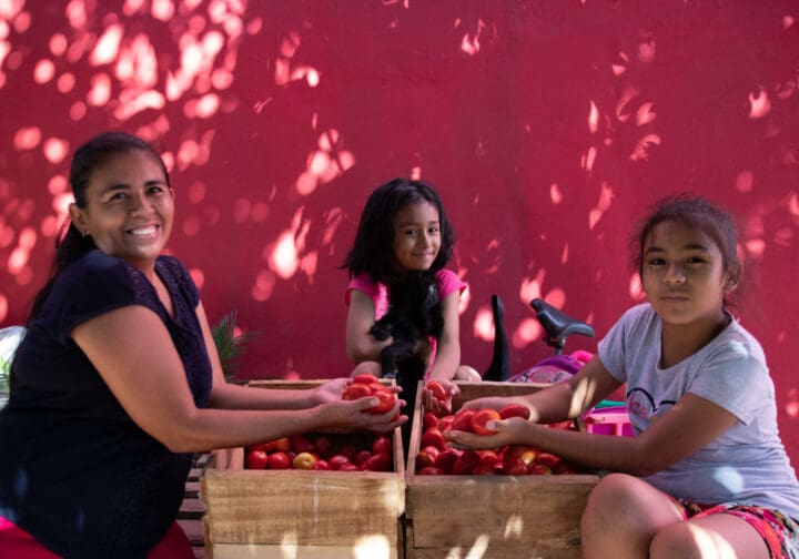 en kvinna från SOS Barnbyars familjestärkande program i Bolivia sitter med sina två döttrar vid två grönsakslådor.