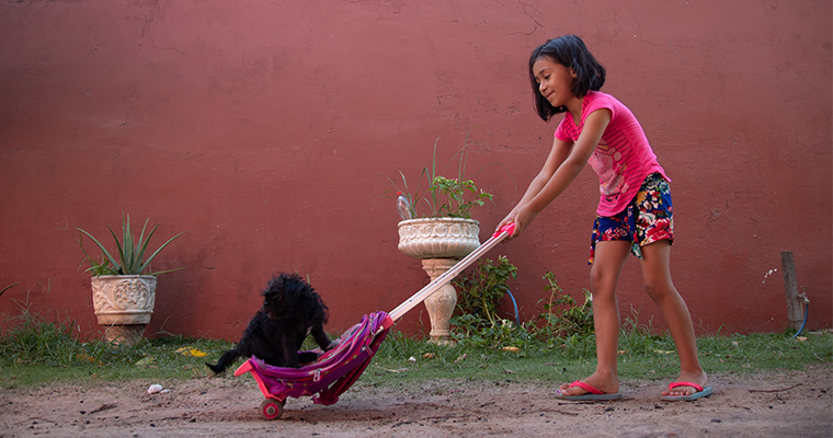 en boliviansk flicka skjutsar en svart hund på en rullväska.