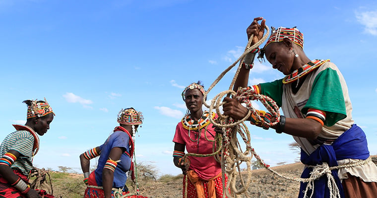 blå himmer och kvinnor i färgstarka tröjor i kenya hämtar vatten i en brunn med rep