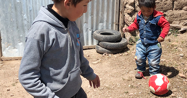 två pojkar leker med en röd och vit boll på grusplan vid några däck