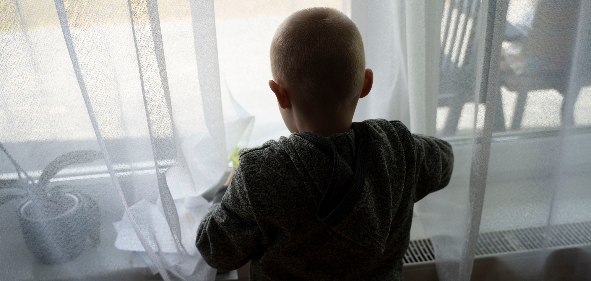 Pojke i motljus tittar ut genom fönstret.