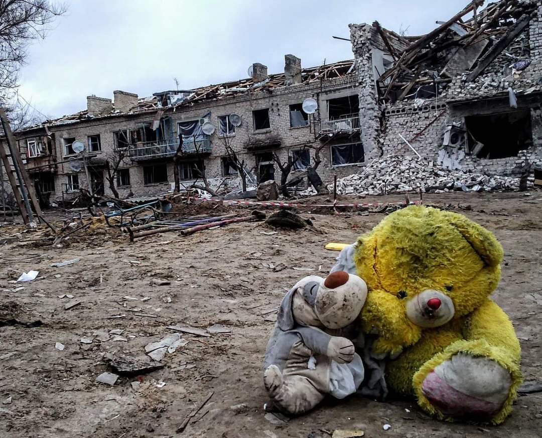 Två gosedjur framför sönderbombade hus i Ukraina.