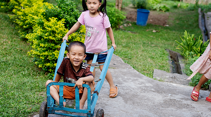 Ett barn kör ett annat barn i en blå liten pirra vagn