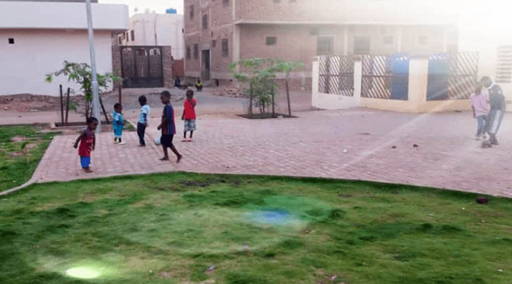 Barn på avstånd leker i motljus bland hus och gräs