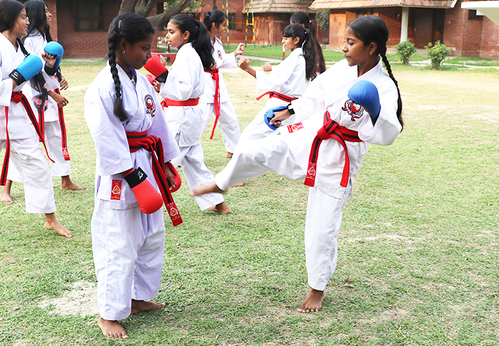 Två flickor i vita kläder och rött skärp på grön gräsmatta utövar karate