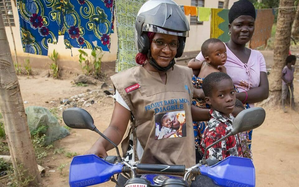 Kvinna på motorcykel, i bakgrunden ser man en mamma och två barn.