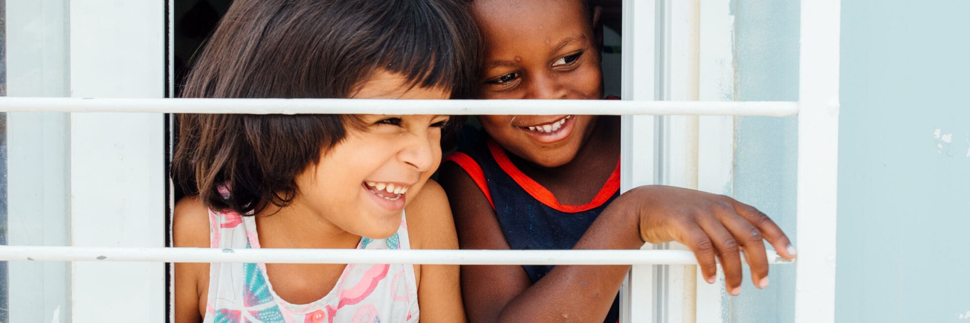 Två barn skrattar och tittar ut genom ett fönster.