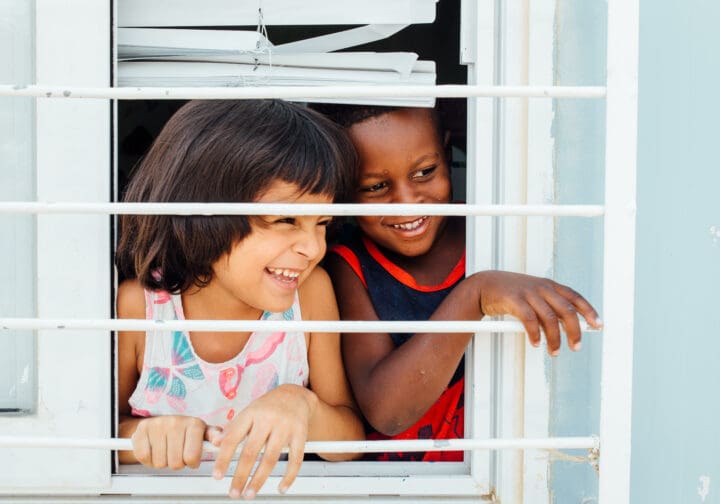 Två barn i SOS Barnbyars program skrattar och tittar ut genom ett fönster.