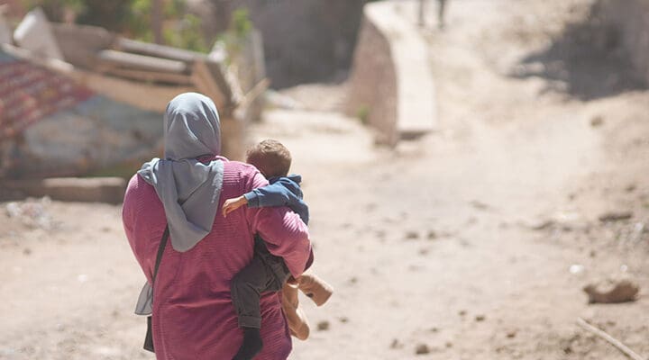 Kvinna syns bakifrån i sjal och bär barn i sina armar