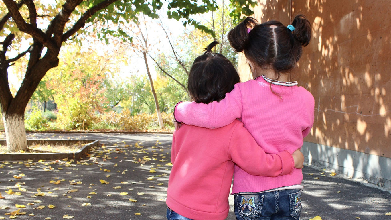 Ryggtavlan av två små flickor i rosa tröjor håller om varandra
