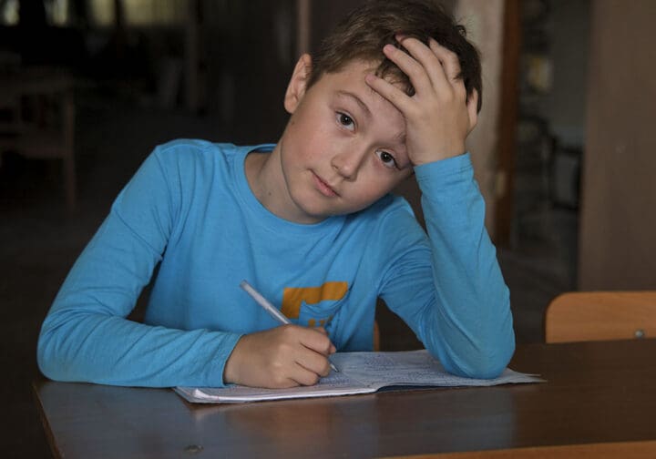 En pojke som sitter vid ett bord och skriver i en anteckningsbok.