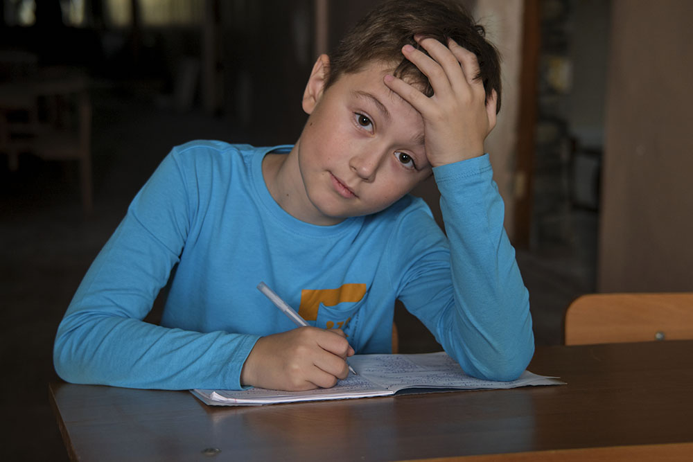 En pojke som sitter vid ett bord och skriver i en anteckningsbok.