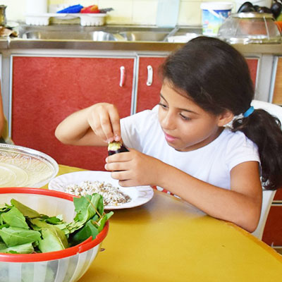 Flicka vid köksbord med en grönsak i handen