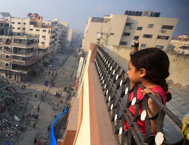 En flicka i Gaza tittar ut över förstörda byggnader.