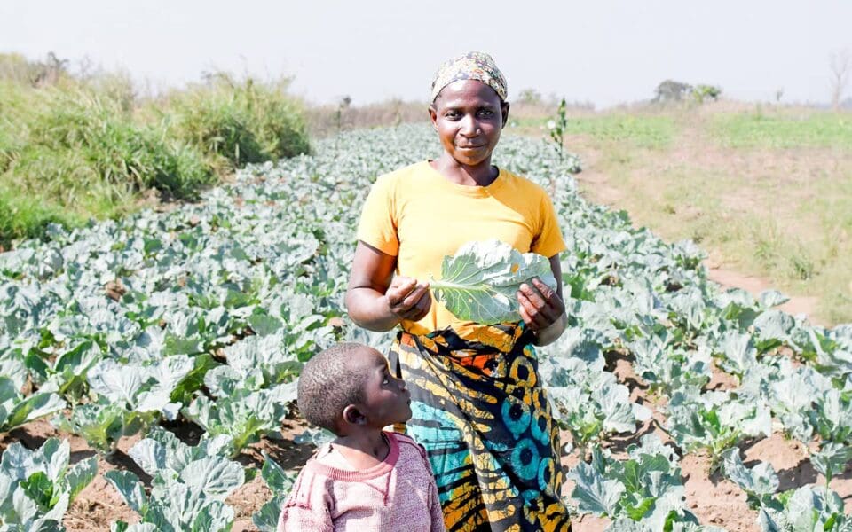 Kvinna och barn står i en odling.