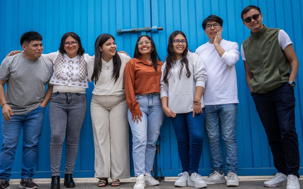 Sju ungdomar står mot en blå vägg