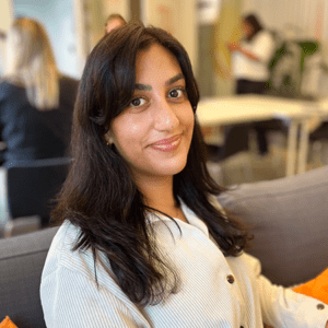 Kvinna i mörkt hår och vit skjorta ler mot kameran