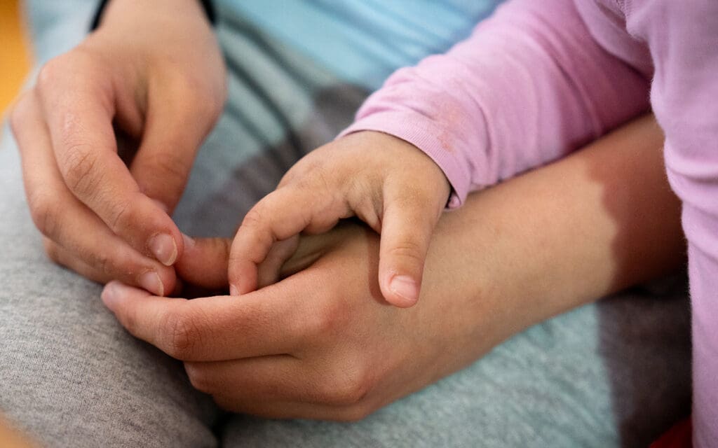 en barnhand håller i en trygg vuxenhand i knät