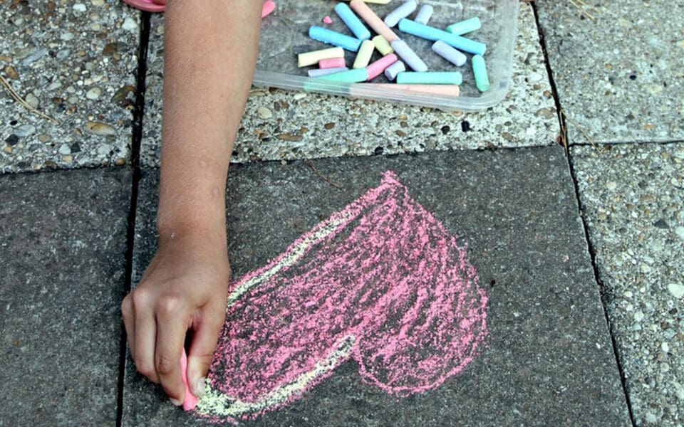 Barnhand ritar ett rosa hjärta i kriat på asfalt