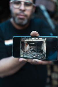 En man håller en mobilkamera som visar bild av nedbrunnet hus 