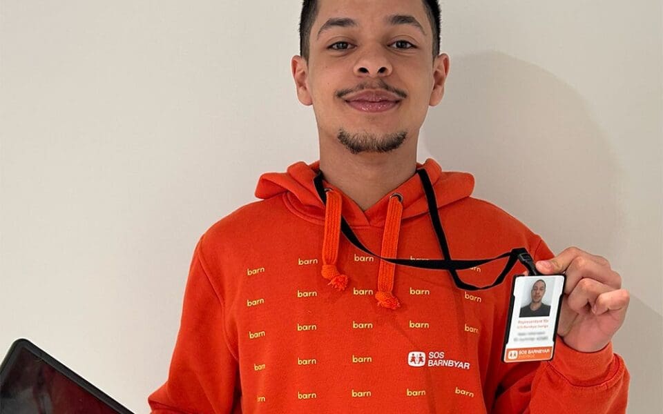 Representant för SOS Barnbyar iklädd orange luvtröja och ID-bricka.