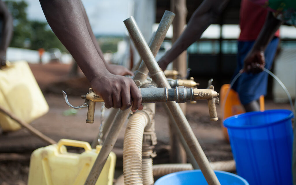 Någon tar vatten i ett flyktingläger i Uganda