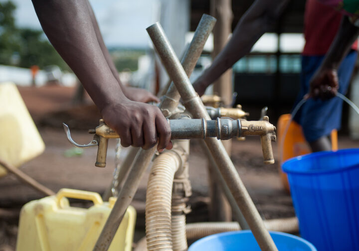 Någon tar vatten i ett flyktingläger i Uganda