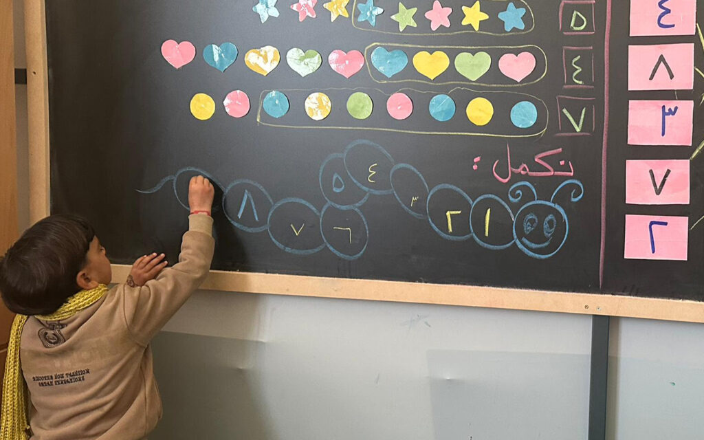 liten pojke bakifrån skriver nåt på svarta tavlan