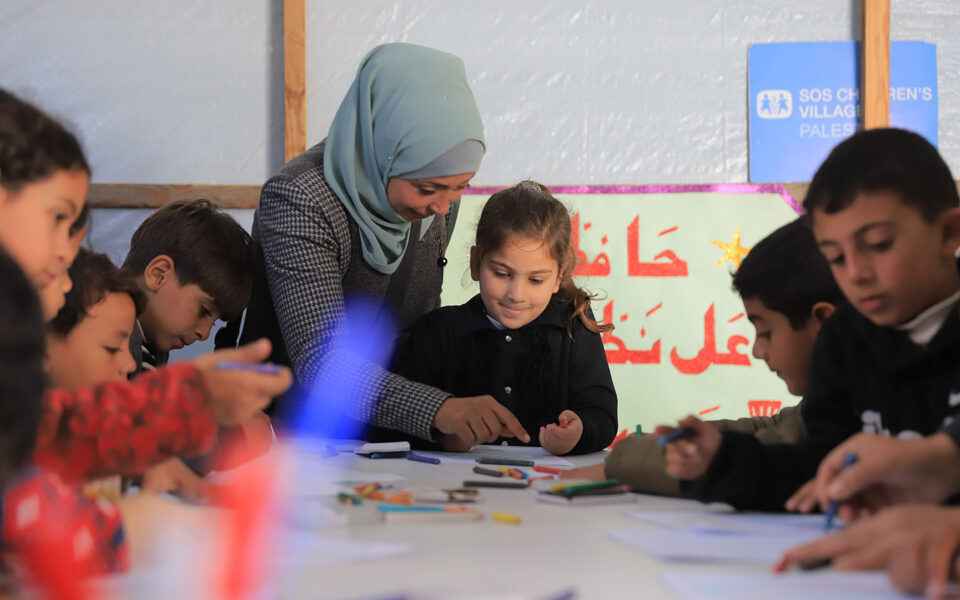 flicka får hjälp av en lärare i ett tillfälligt klassrum i gaza