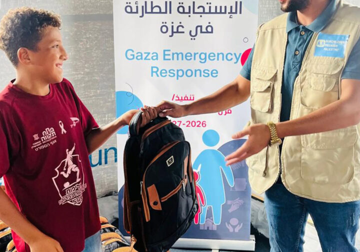 en pojke tar emot en ryggsäck av personal på SOS barnbyar i läger i gaza